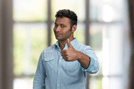 Handsome young man looking at camera and giving thumb up gesture. Attractive indian guy showing thumb up symbol.の写真素材