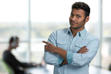 Handsome Indian businessman pointing at copy space. Office interior blur background. Product advertisement concept.の写真素材