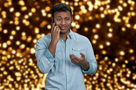 Young handsome man wearing blue shirt talking on mobile phone. Festive bokeh lights in the background.の写真素材
