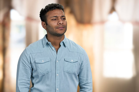 Young thoughtful man standing on interior blur background. Serious pensive man looking aside.の写真素材