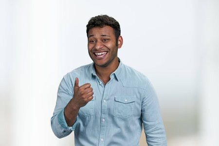 Young laughing man showing thumb up gesture standing on blurred background. Funny crazy joke. Human emotions and expressions.の写真素材
