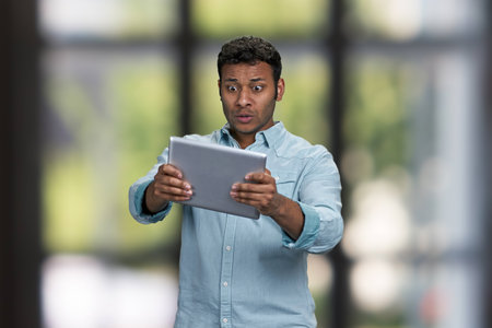 Surprised indian man using digital tablet pc. Interior blur background.の写真素材