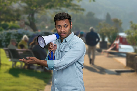 Young indian man holding megaphone and showing something with hand. Blur crowded city street in the background.の写真素材