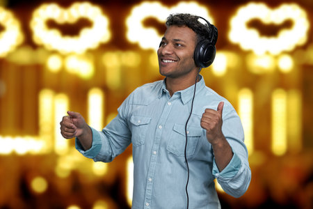 Handsome young man is dancing while listening music with headphones. Golden bokeh lights in the...