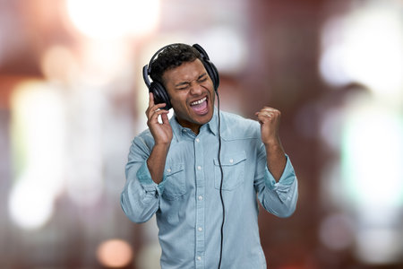 Ecstatic young man enjoying listening to music with headphones. Abstract bokeh background.の写真素材