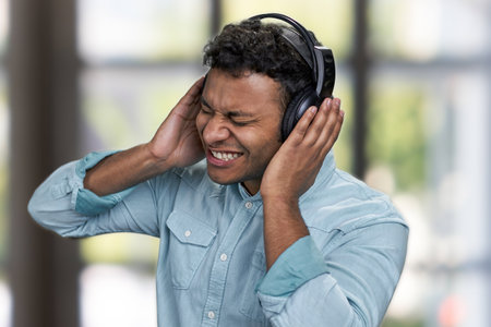 Young expressive man listening to music with headphones. Interior blur background.の写真素材