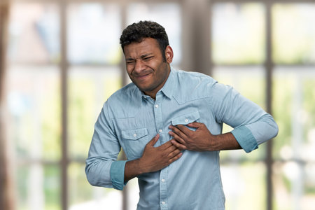 Young indian man suffering from heart ache. Blur interior background. Heart disease concept.の写真素材