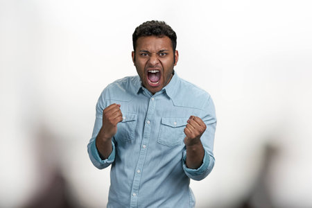 Emotional young man clenched fists and screaming in aggression. Furious indian man on blurred background.の写真素材