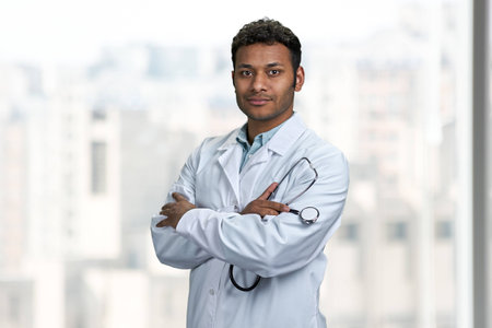 Young confident indian doctor with stethoscope looking at camera standing with arms crossed. People, medicine and occupation concept.の写真素材