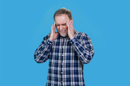 Aged senior man toucing his head with both hands. Isolated on blue.の写真素材