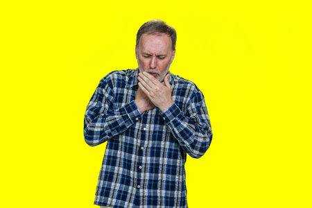 Portrait of a sick coughing mature senior man. Isolated on yellow.の写真素材
