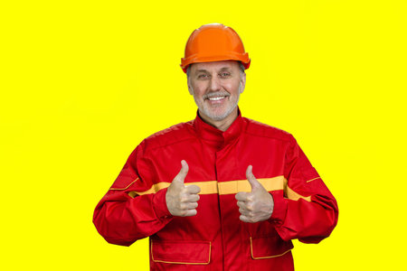 Portrait of happy smiling construction worker gives both thumbs up. Isolated on vivid yellow.の写真素材