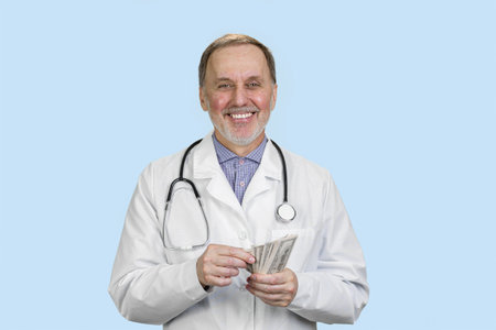 Portrait of a smiling male doctor is counting money. Isolated on blue.の写真素材