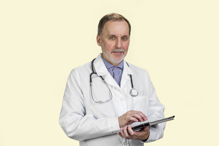 Aged senior male doctor holding digital tablet in hands. Isolated on white.