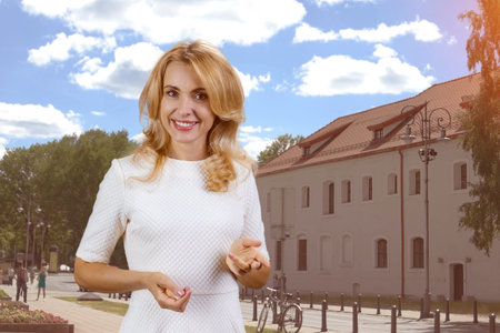 Portrait of cheerful blonde mature woman talking you you and gesturing. Urban city street and buildings in the background.の写真素材