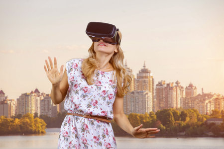 Portrait of amazed blonde mature woman in vr headset outdoors. City river in the background.の写真素材
