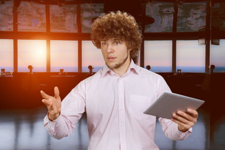 Handsome young entrepreneur with curly hair standing with tablet pc device giving a speech. Indoor restaurant setting in the background.の写真素材