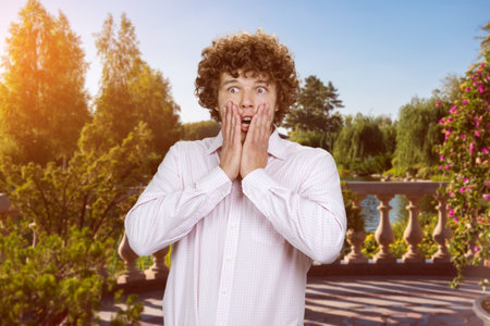 Portrait of scared shocked young man with curly hair outdoors. City park in the background.の写真素材