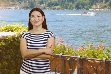 Young asian woman with folded arms standing outdoors. Garden and sea water background.の写真素材