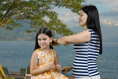 Portrait of brunette woman is combing a little girl outdoors. Sea resort vacation background.の写真素材