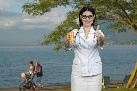 Young smiling female doctor is giving a can of medicine and showing thumb up. Blue seascape background.の写真素材