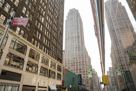 Tall buildings line a narrow street in Midtown Manhattan. One facade reflects the skyline in its mirrored glass.の写真素材