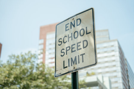 A traffic sign stating End School Speed Limit stands against the backdrop of modern city buildings....