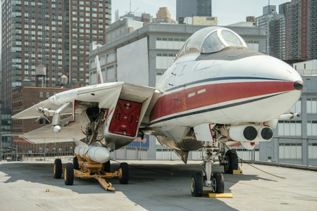 A military fighter jet is parked on a rooftop with buildings in the background. The aircraft is...