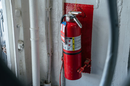 A red fire extinguisher is securely mounted on a white metal wall with a red backplate. It is placed...