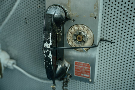 A vintage black rotary dial telephone is mounted on a perforated metal wall inside a ship. The phone...