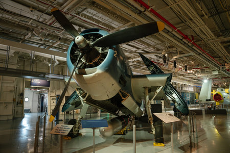 A restored vintage propeller aircraft is showcased indoors with its wings partially folded and a torpedo mounted underneath. The museum lighting highlights mechanical details and historical significance.の写真素材