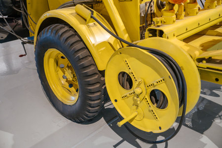 This detailed image shows the large rubber tire and circular cable reel of a yellow utility trailer....