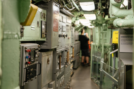 The corridor of a U.S. Navy submarine is lined with vintage control panels and equipment. A visitor...
