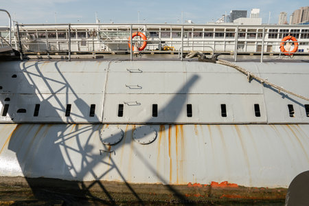 Detailed view of a grey military submarine hull with rust streaks, shadows of railing structures,...