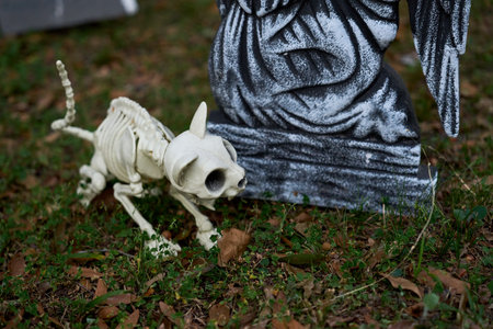 A bony cat skeleton crouches near a stone tomb marker. The white bones and grave statue create a...