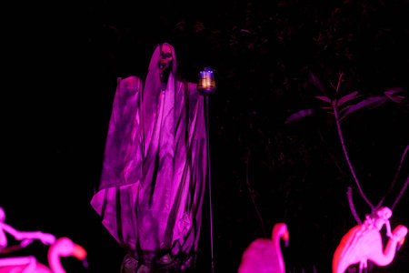 Two tall hooded reapers with lanterns glow purple in a spooky lawn scene. The nighttime haunted...