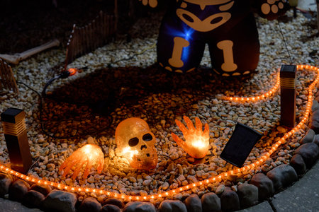 Glowing skull and hands sit on gravel with orange rope lights at night. Spooky Halloween yard...