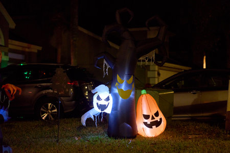 A glowing ghost, carved-face pumpkin, and twisted spooky tree inflatables stand on a suburban lawn...
