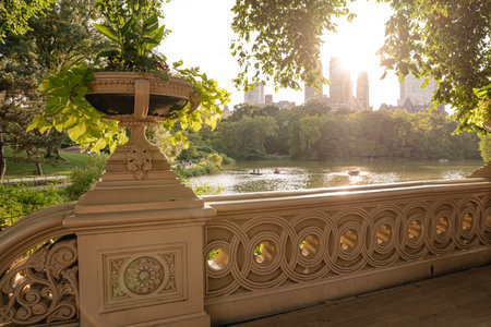 A decorative flower planter sits atop Bow Bridge, with a scenic view of the lake and Manhattan...