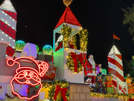A large Santa decoration stands on a lighted tower with red ribbons and Christmas ornaments. The...