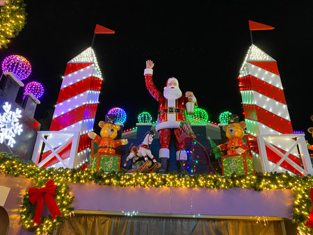 Large Santa Claus figure stands between tall red towers decorated with garlands, ribbons, and...