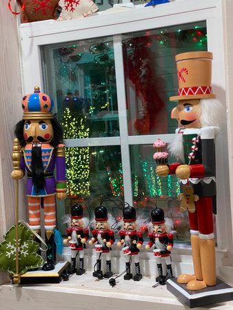 Colorful nutcracker figurines stand on a window sill with glowing holiday reflections. The festive...