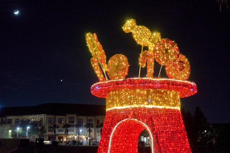 A candy-topped light sculpture sparkles in red and gold against the dark night sky. The festive arch shines with peppermint and lollipop shapes in a city plaza.の写真素材
