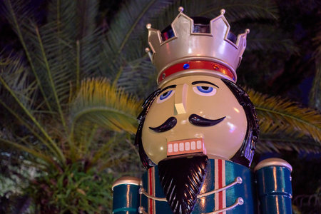 A decorative nutcracker stands under palm fronds with festive lights at night. The holiday statue shows Christmas tradition in a warm city park.の写真素材