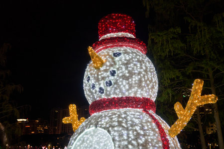 A bright LED snowman with a red hat and scarf glows at night. Holiday decoration brings cheerful winter spirit to the city.の写真素材