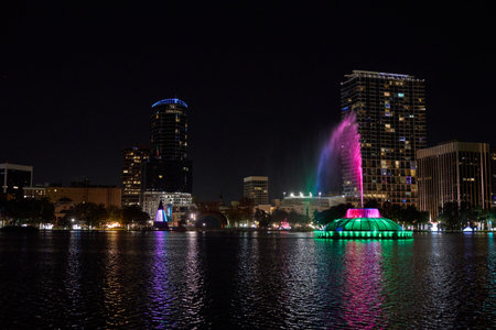 A wide city panorama shows a glowing fountain and colorful lights across the water. Towers and high-rises shine in a calm night scene.の写真素材