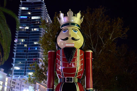 A red nutcracker holiday statue stands under city skyscrapers at night. Festive Christmas decoration...