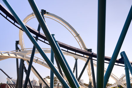 Interlacing loops and supports form an abstract network of steel. The modern roller coaster design stands out against a clear blue sky.の写真素材