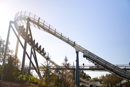 Orlando, Florida, USA - 11.15.2024: A coaster train descends a curving track past tall columns. Sunlight and trees frame the dynamic theme park moment.のeditorial素材