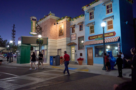 Orlando, Florida, USA - 11.15.2024: Visitors walk along a Sesame Street themed city block decorated with Christmas garlands and bright streetlights. Cookie Monster greets children outside the Sunny Day Salon on a warm night.のeditorial素材
